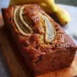 Slice of healthy banana bread topped with nuts and banana slices