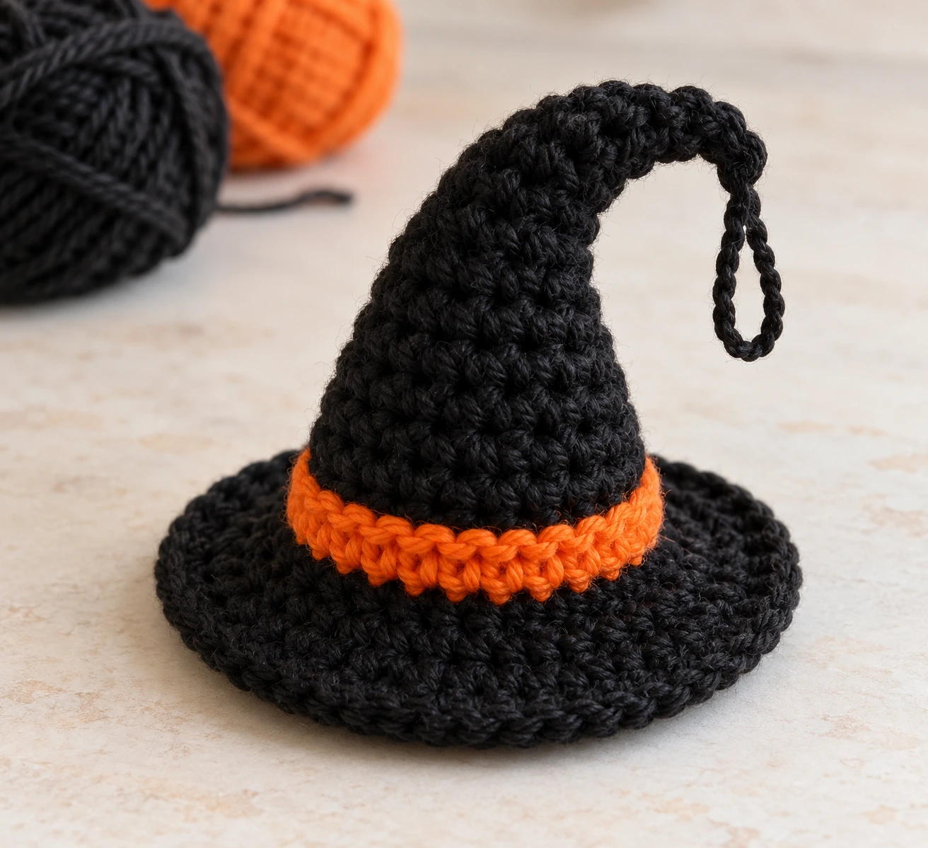 Small black crochet witch hat with an orange band and a chain hanging loop